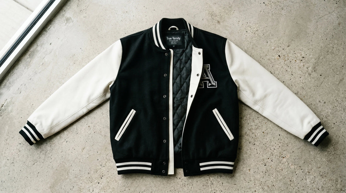 Premium two-tone black and white baseball jacket flat lay showing snap-button front, rib-knit collar and contrasting sleeves
