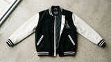 Premium two-tone black and white baseball jacket flat lay showing snap-button front, rib-knit collar and contrasting sleeves