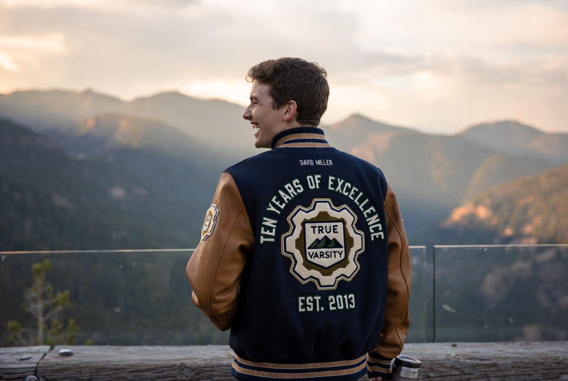 Man wearing a custom varsity jacket with branded back design overlooking a mountain view.
