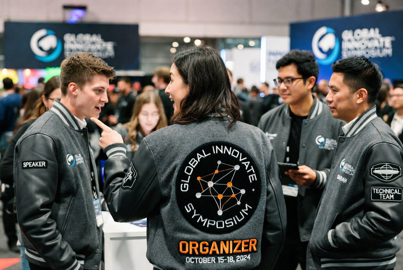 Event staff wearing branded varsity jackets while networking at a busy conference expo.