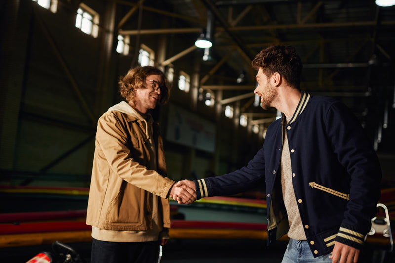 Two men shaking hands in casual jackets during a wholesale partnership meeting.