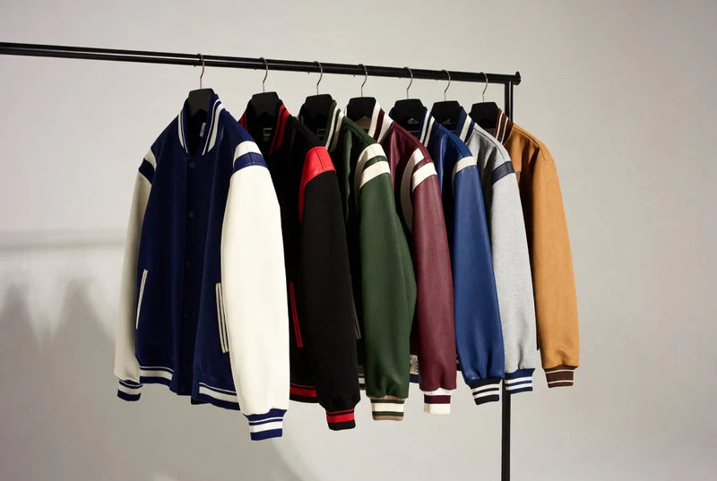 Collection of colorful letterman jackets hanging on a clothing rack in a studio.